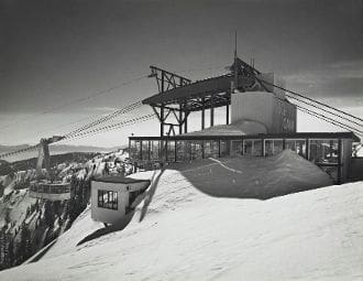 A ski lift on top of a mountain with people standing around.