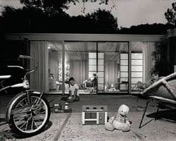 A black and white photo of a house with children and a bicycle.