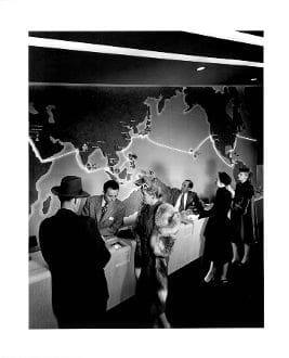 A group of people standing around tables in front of a map.