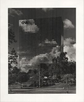 A black and white photo of trees, clouds and buildings.