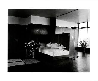 A black and white photo of a bedroom with a bed, nightstand, and window.