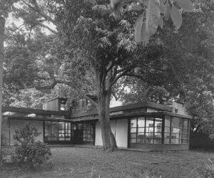 A black and white photo of a tree in front of a house.