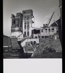 A black and white photograph of a building being demolished.