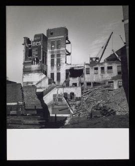 A black and white photograph of a building being demolished.