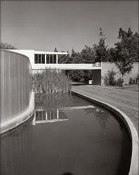 A black and white photo of a pond in front of a house.