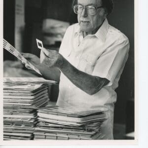Elderly man reviewing photographs in a workspace.